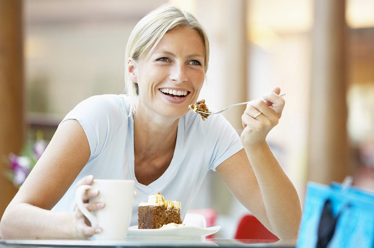 Frau genießt Kuchen und Kaffee mit Lächeln – Pause im Café.