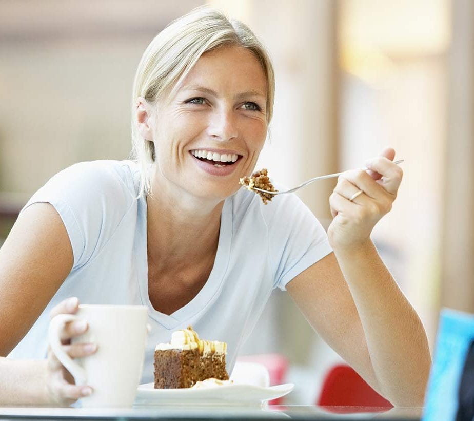 Frau genießt Kuchen und Kaffee mit Lächeln – Pause im Café.