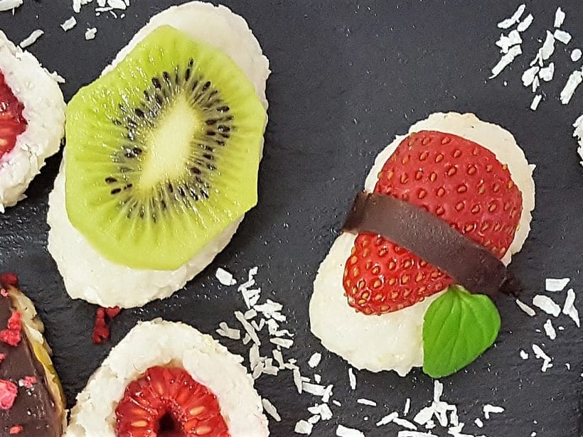 Fruchtige Kokos-Sushi mit Kiwi und Erdbeere auf schwarzer Platte, verziert mit Kokosraspeln. Datei: sushi-dessert.jpg