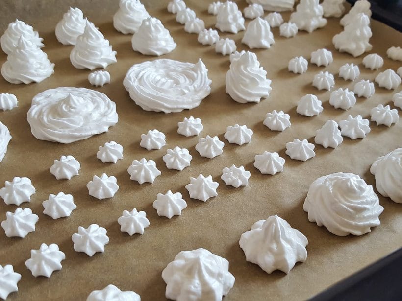 Frische Baiser auf einem Backblech, bereit zum Backen im Ofen. Perfekte süße Leckereien für Desserts und Dekorationen.