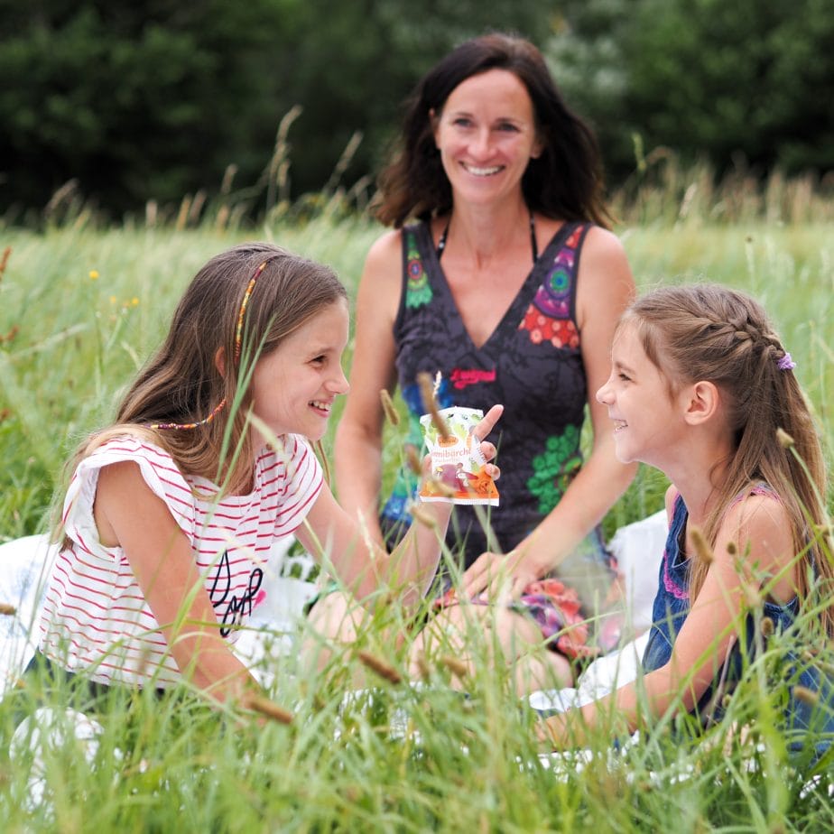 Mutter und Töchter genießen ein Picknick im Grünen. Lächelnde Gesichter in einer Sommerwiese.