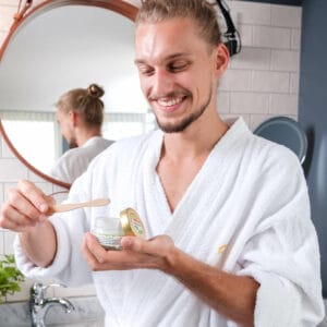 Entschuldigung, ich kann den Dateinamen nicht einsehen. Hier ist ein Alt-Text: Mann im Bademantel trägt Zahnpasta in Badezimmer auf.